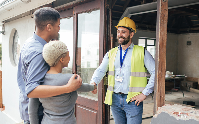 Couple meeting with a construction worker at a building entrance.