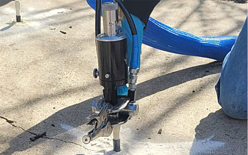 Worker drilling into concrete with a gauge and hoses attached to machinery.