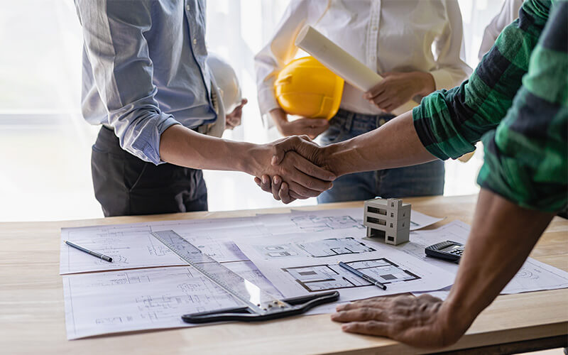 Architects shaking hands over senior living community blueprints on table.