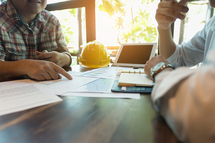 Two people discussing plans with documents and a hard hat on the table.